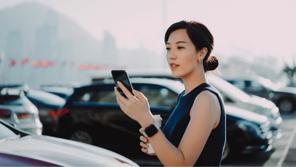 woman looking at phone with coffee in a parking lot